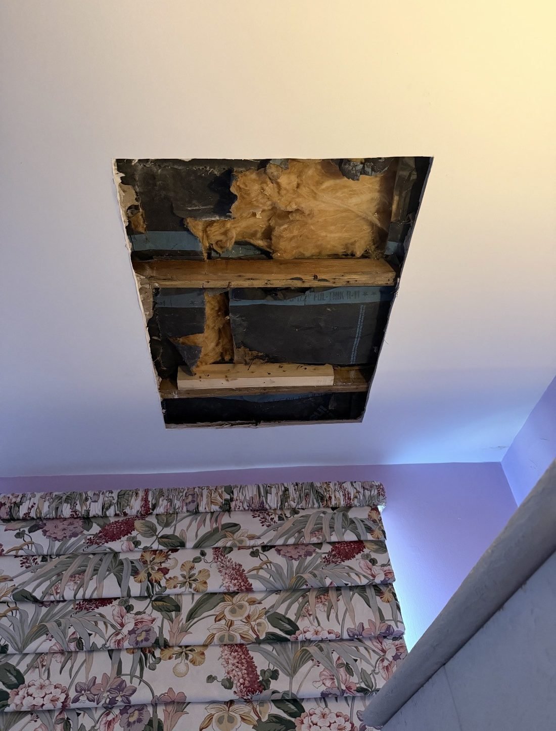 A bedroom ceiling cut open to the joists and insulation before the repair